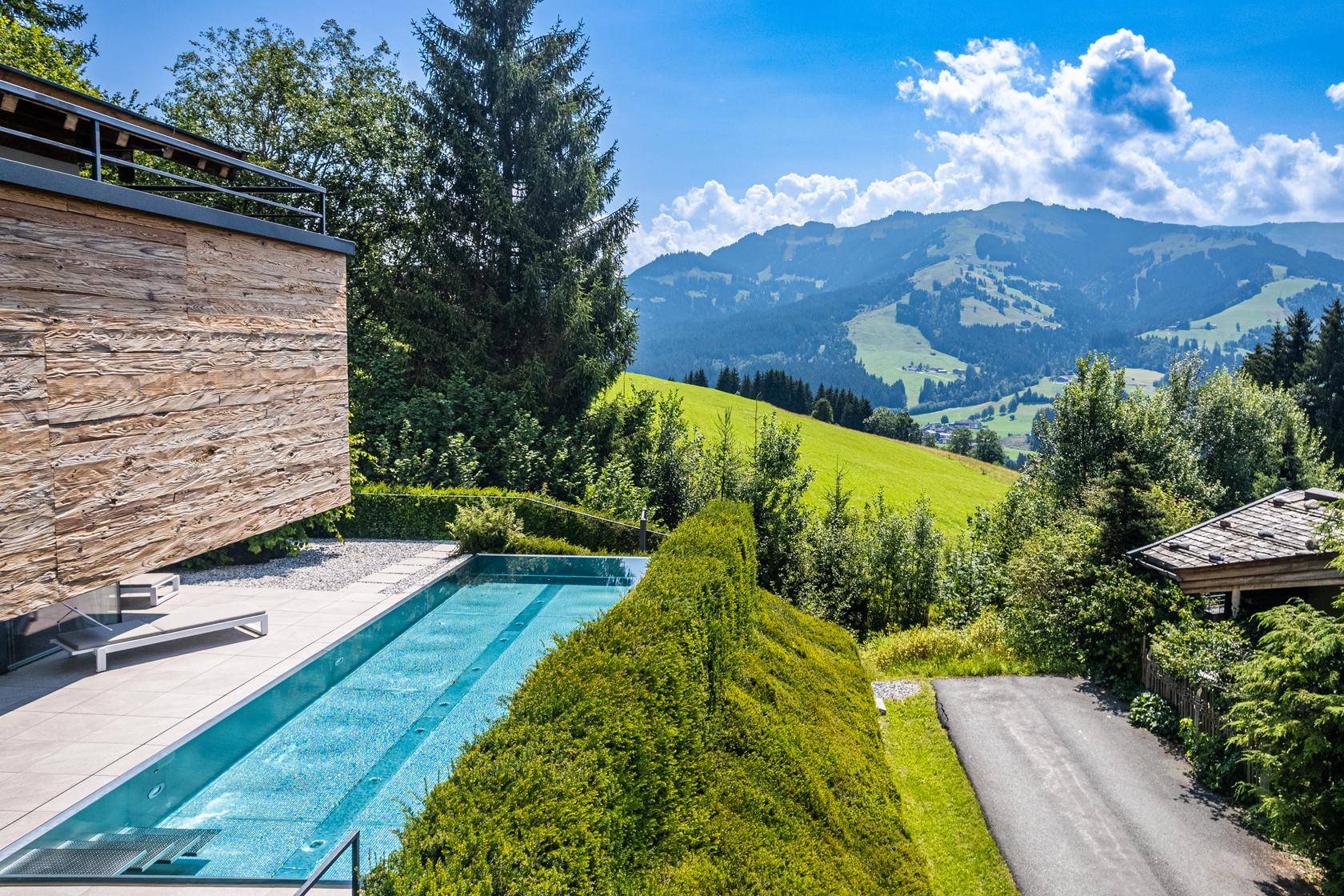 Infinity-Pool mit Liegebereich und weitem Blick auf die grüne Berglandschaft.