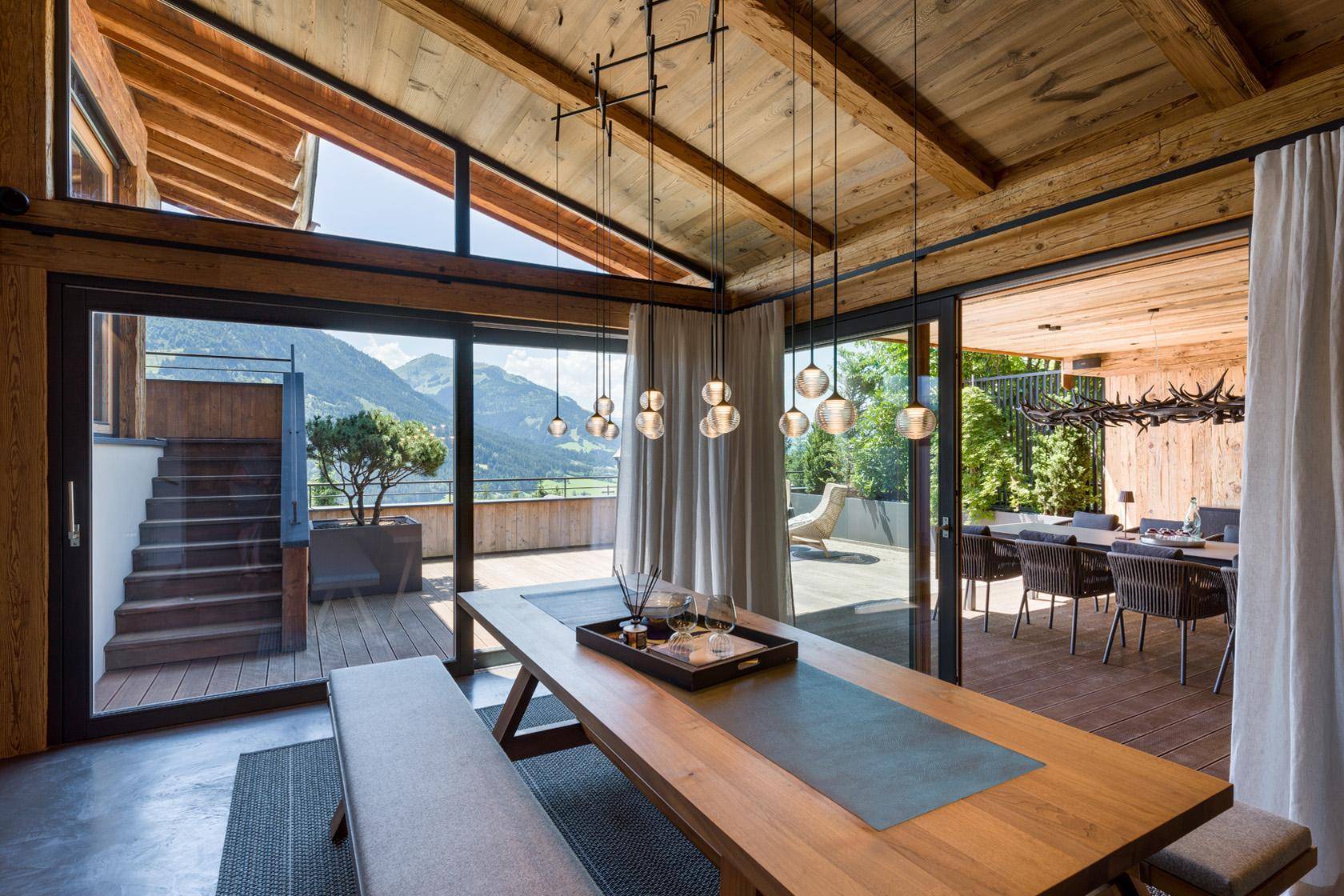 Heller Essbereich mit Holztisch, Zugang zur Terrasse und Blick auf die umliegende Berglandschaft.