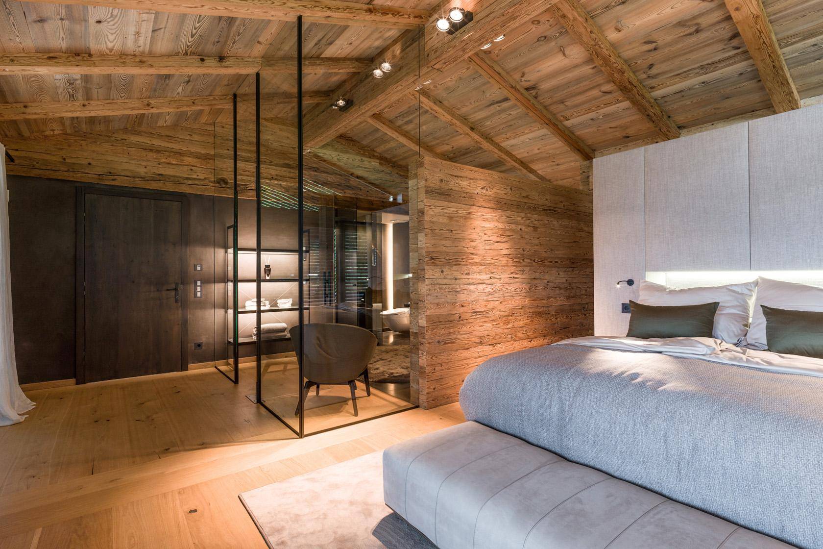 Geräumiges Schlafzimmer mit Holzwänden, Holzbalkendecke und offenem Badezimmerbereich.