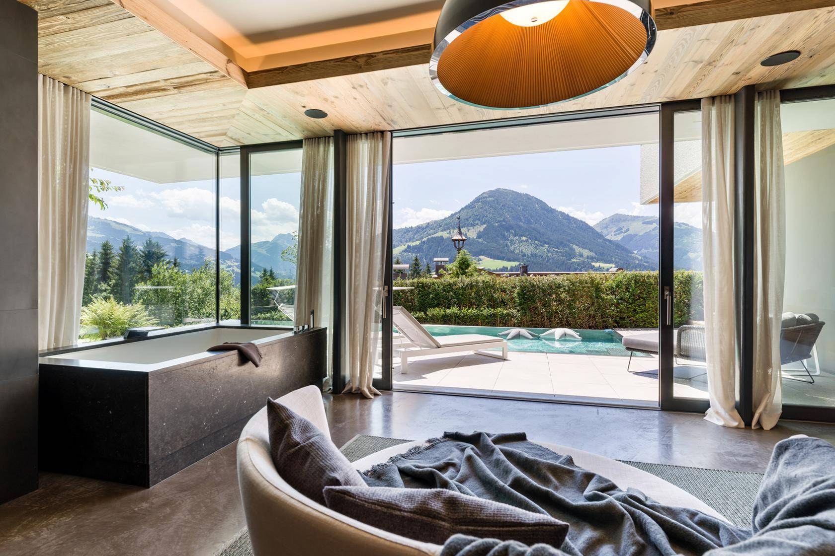 Luxuriöser Badebereich mit Badewanne und Panoramablick auf den Pool und die Berge.