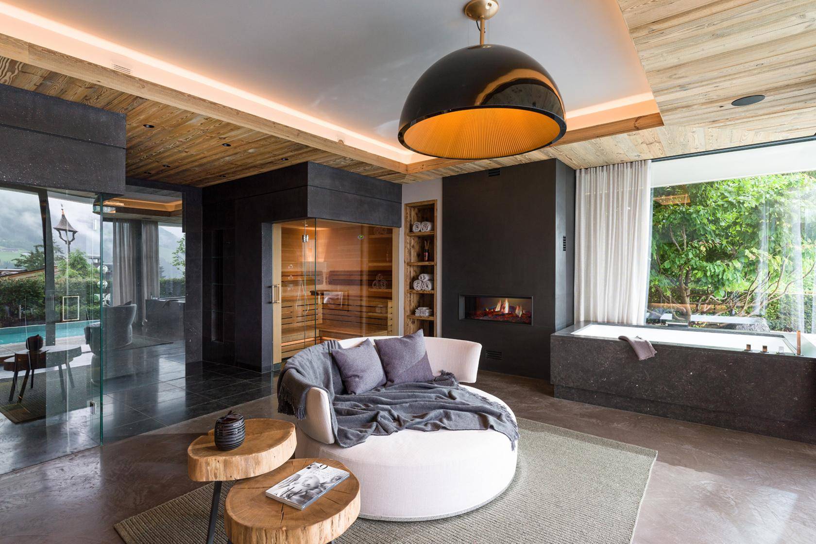 Exklusiver Wellnessbereich mit Sauna, Badewanne, Kamin und Blick auf den Pool.