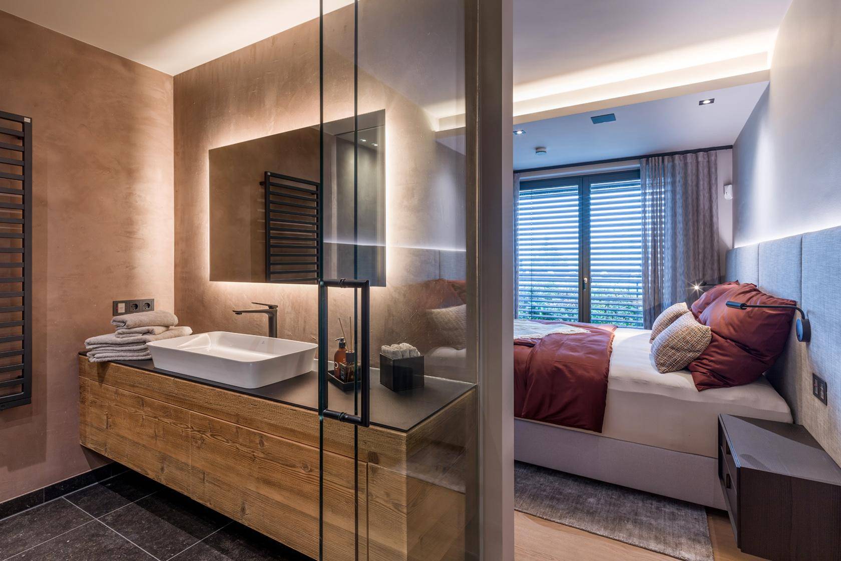 Modernes Schlafzimmer mit Waschtisch, beleuchtetem Spiegel und Zugang zum Balkon.