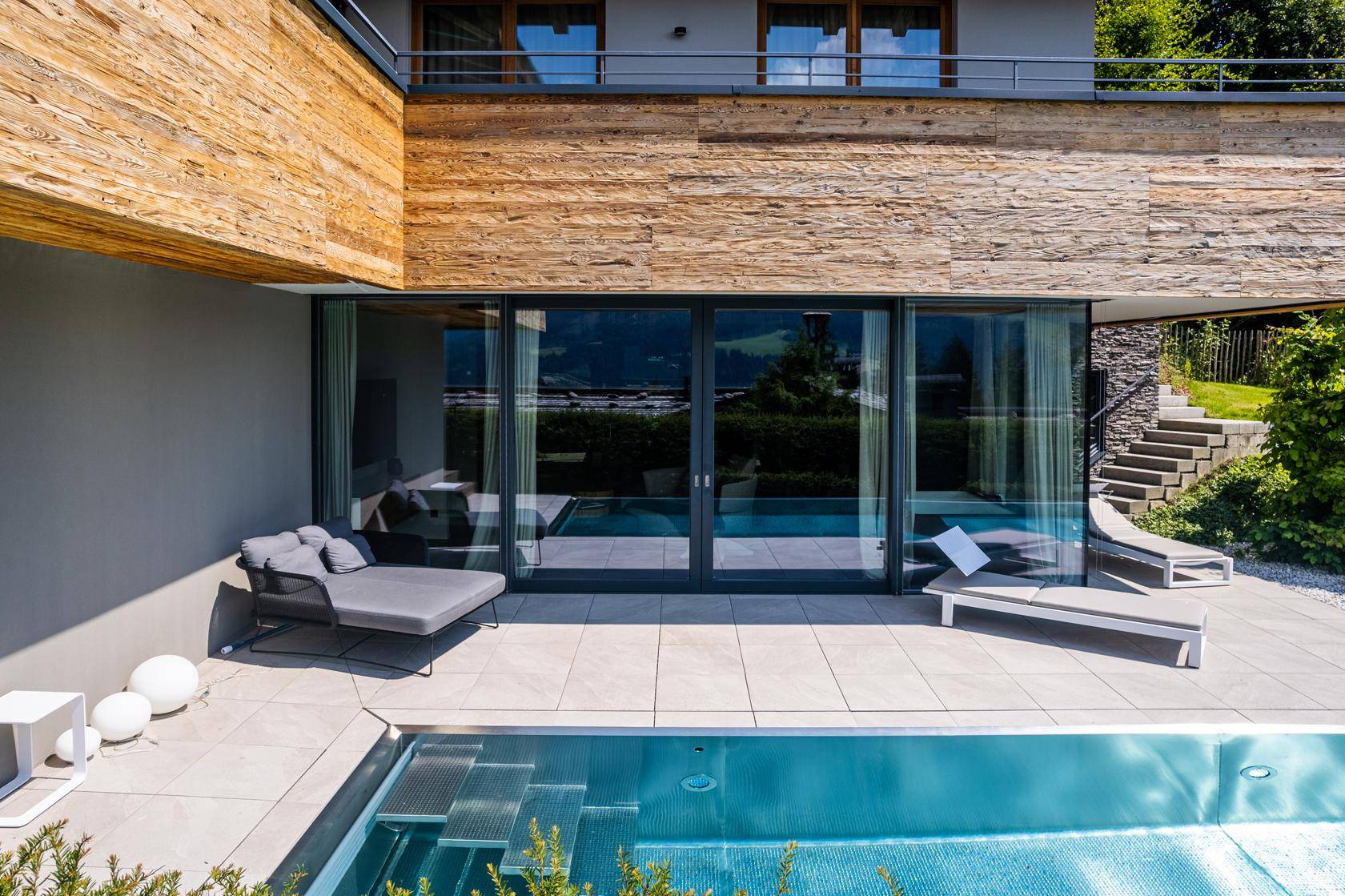 Terrasse mit Infinity-Pool und Liegebereich, umgeben von moderner Architektur.