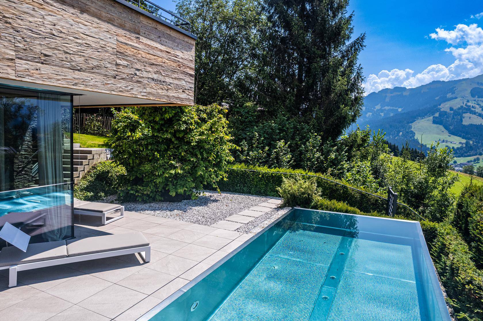 Infinity-Pool mit Liegestühlen und Blick auf die grüne Hügellandschaft.
