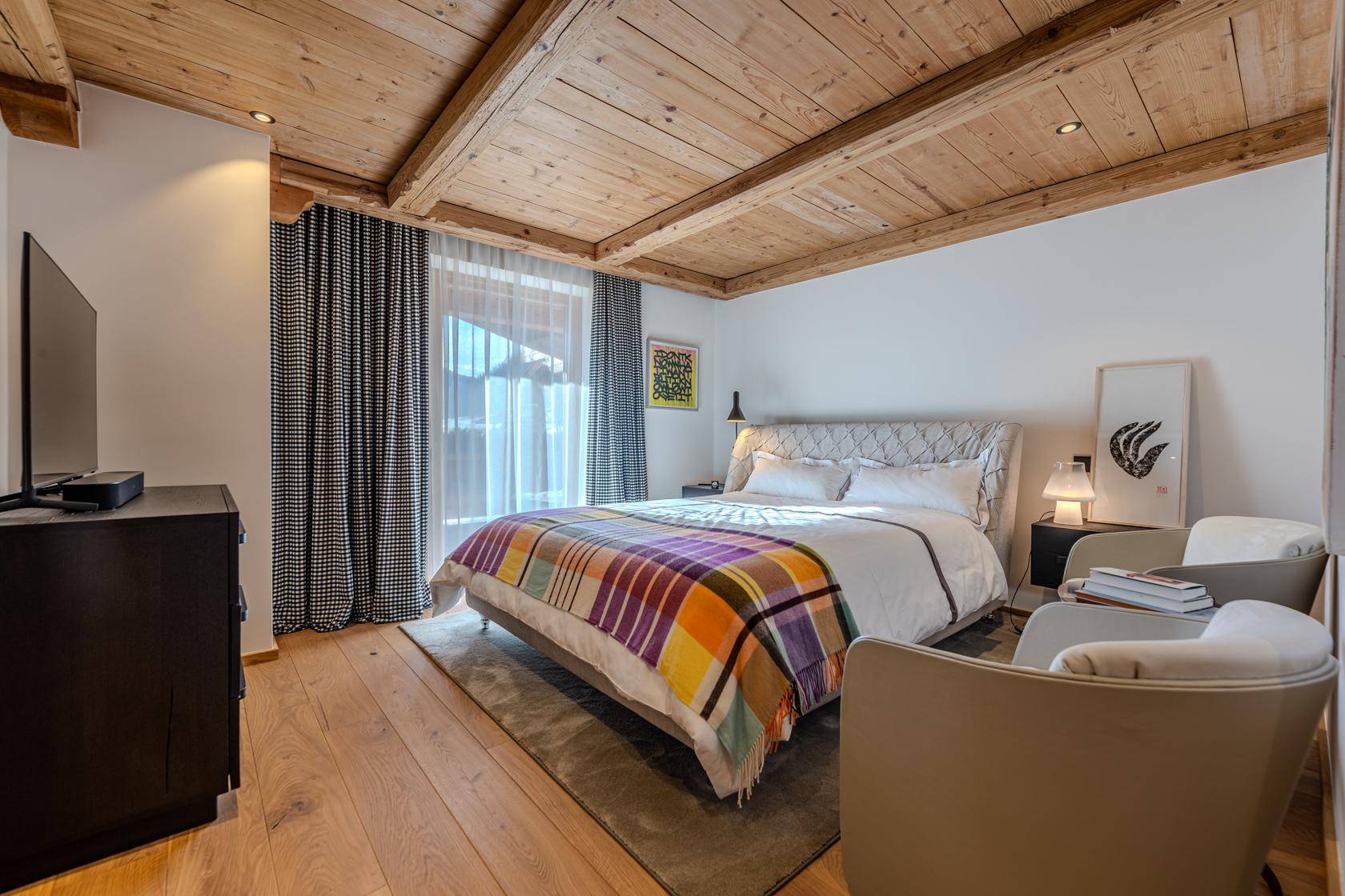 Gemütliches Schlafzimmer mit Holzbalkendecke, Parkettboden und Zugang zum Balkon.