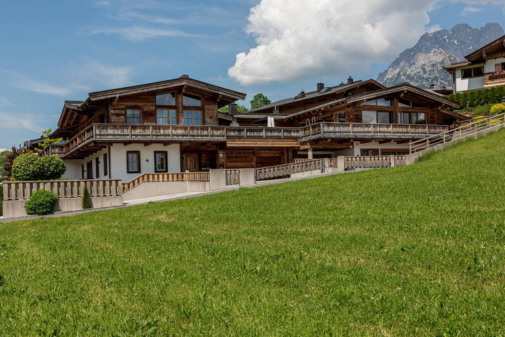 Traditionelles Holzchalet mit mehreren Balkonen und Blick auf die Berge in grüner Umgebung.