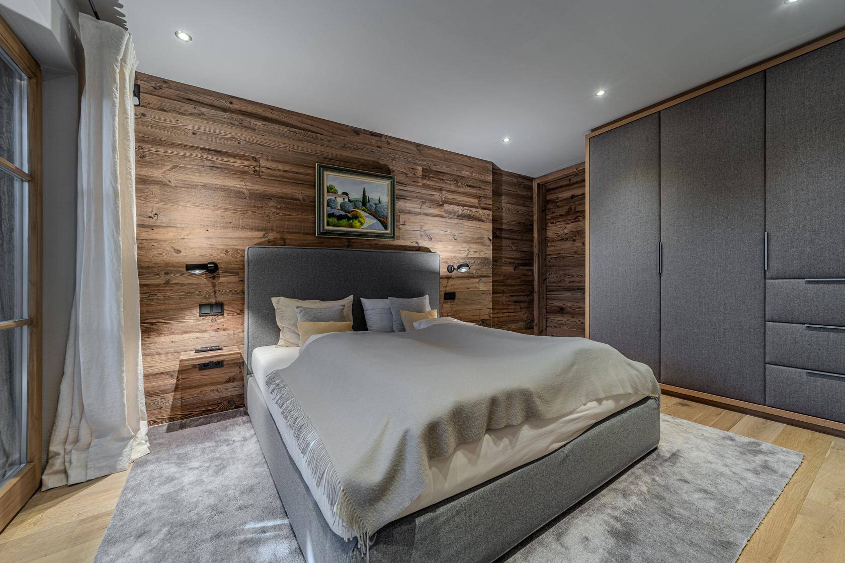 Gemütliches Schlafzimmer mit Holzwand, großem Bett und integrierten Kleiderschränken, in einem modernen Chalet-Stil.