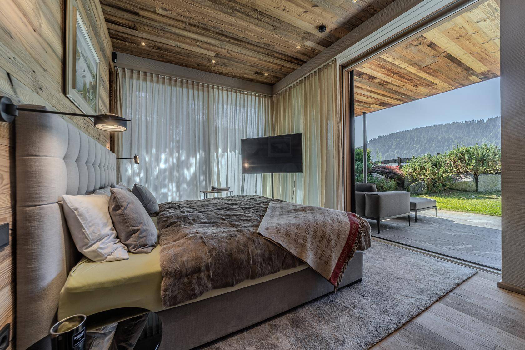 Elegantes Schlafzimmer mit Holzwänden, großem Bett und direktem Zugang zu einer privaten Terrasse mit Gartenblick.