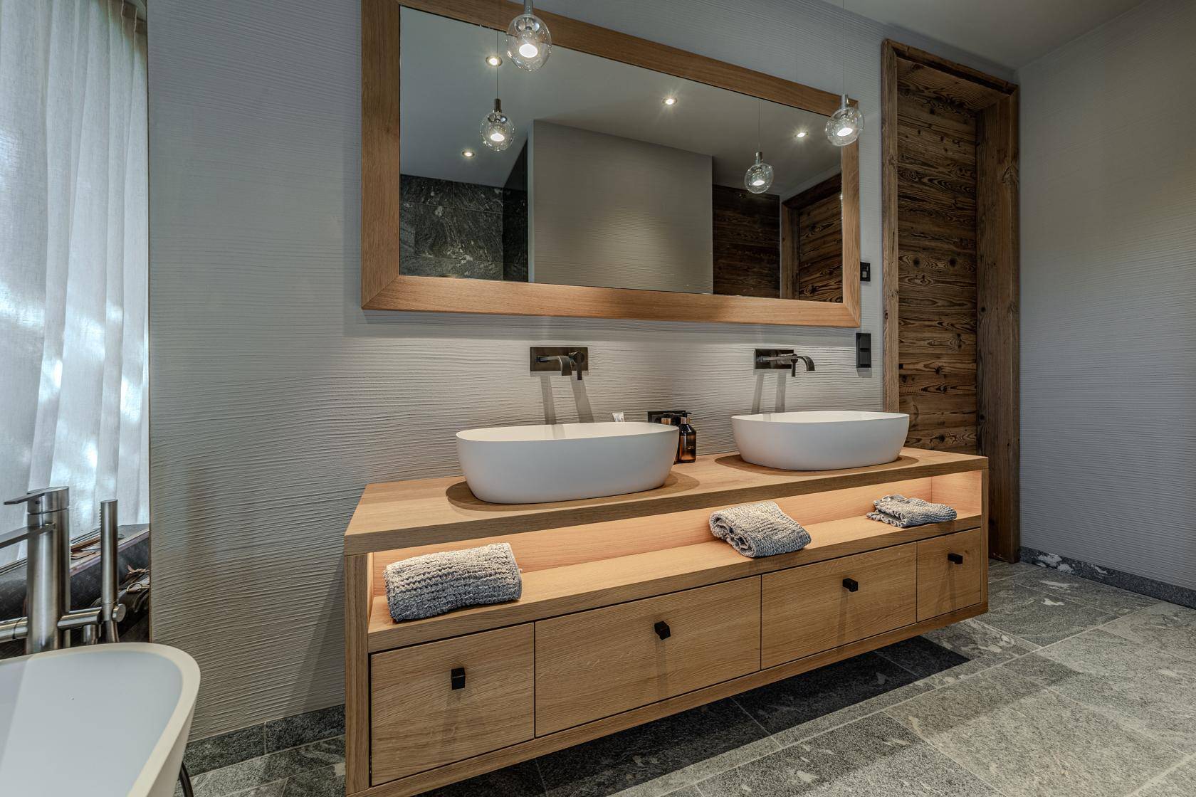 Stilvolles Badezimmer mit Doppelwaschbecken, großem Spiegel und modernen Armaturen, kombiniert mit Holzelementen.
