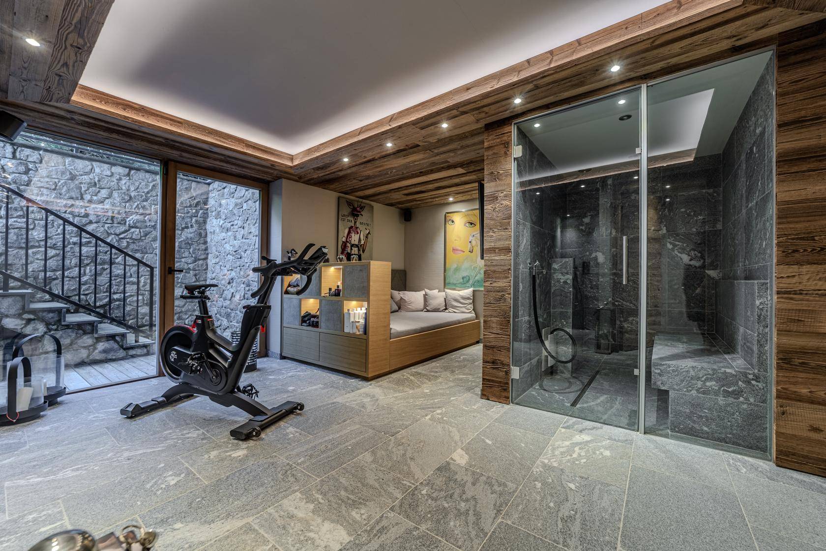 Wellnessbereich mit Fitnessgeräten, Dampfdusche und Zugang zu einem Außenbereich, ideal für Entspannung und Sport.