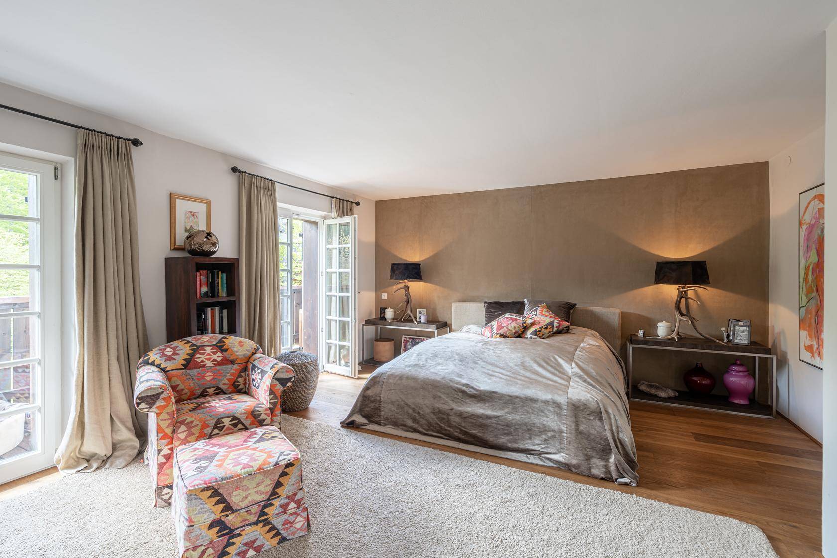 Geräumiges Schlafzimmer mit Balkonzugang, Holzboden und bequemer Sitzecke.