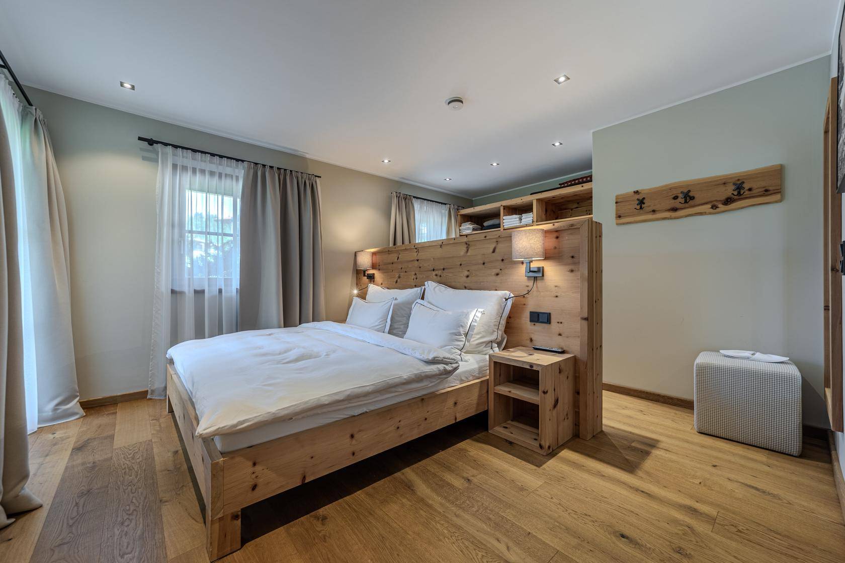 Gemütliches Schlafzimmer mit Holzbett, Holzboden und natürlichem Licht durch die Fenster.