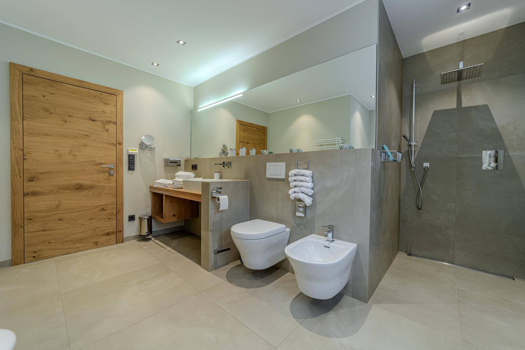 Modernes Badezimmer mit ebenerdiger Dusche, Wand-WC, Bidet und großem Spiegel.