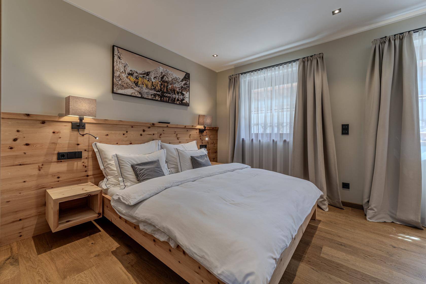 Helles Schlafzimmer mit Holzbett, Holzboden und Bergbild an der Wand für eine gemütliche Atmosphäre.