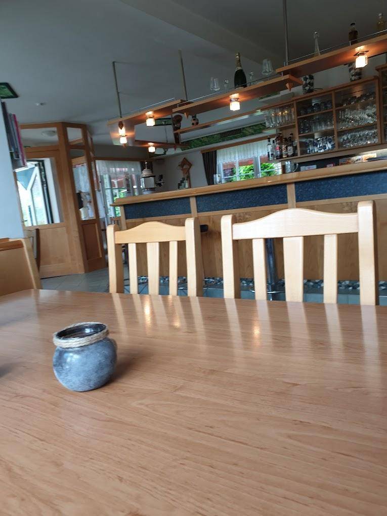 Innenbereich mit Holztischen, Stühlen und einer Bar im Hintergrund, die Gläser und Flaschen präsentiert.