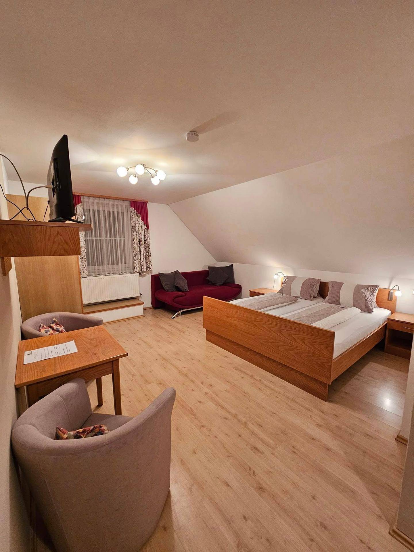 Helles Schlafzimmer mit Doppelbett, bequemen Sesseln, Tisch und Fernseher unter einer Dachschräge.