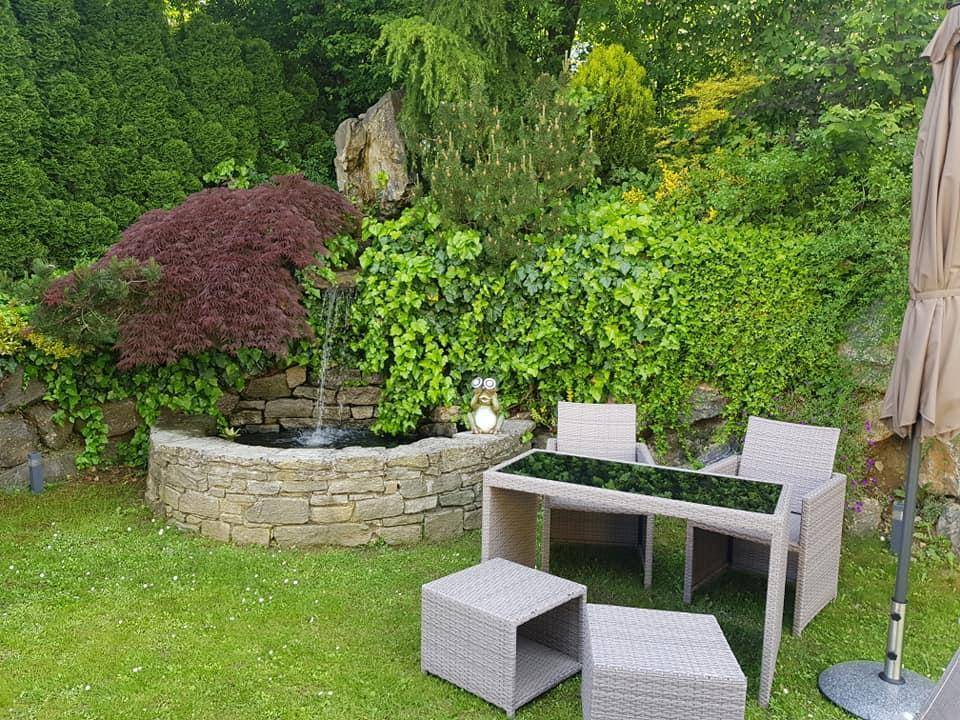 Idyllischer Gartenbereich mit Steinfbrunnen, üppiger Bepflanzung und bequemen Outdoor-Sitzmöbeln.