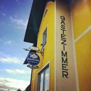 Seitenansicht eines gelben Gebäudes mit einem Schild für "Gästezimmer" und einem Brauerei-Logo.