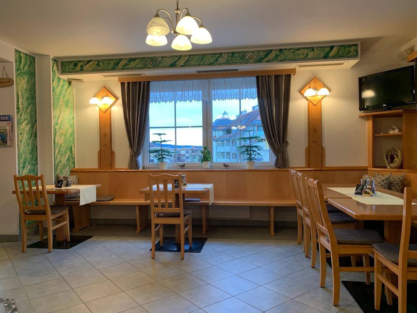 Traditioneller Speisesaal mit Holzbänken, Tischen und Stühlen, hellen Fliesenböden und großen Fenstern.
