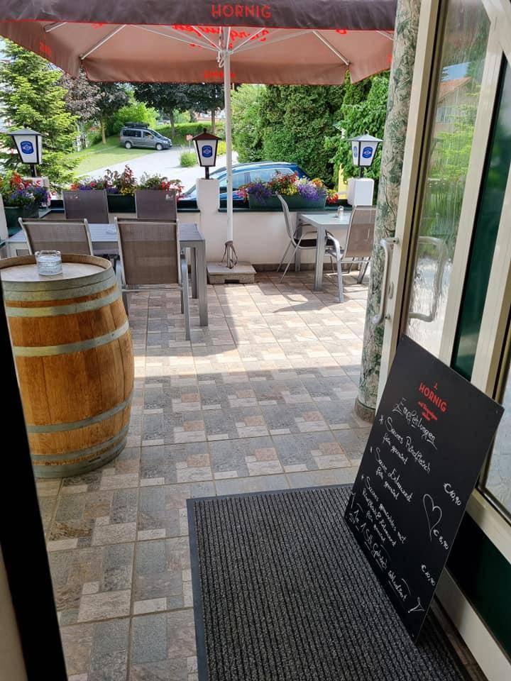 Eingangsbereich zur Terrasse mit gepflastertem Boden, einem Weinfass als Dekoration und einer Menütafel.
