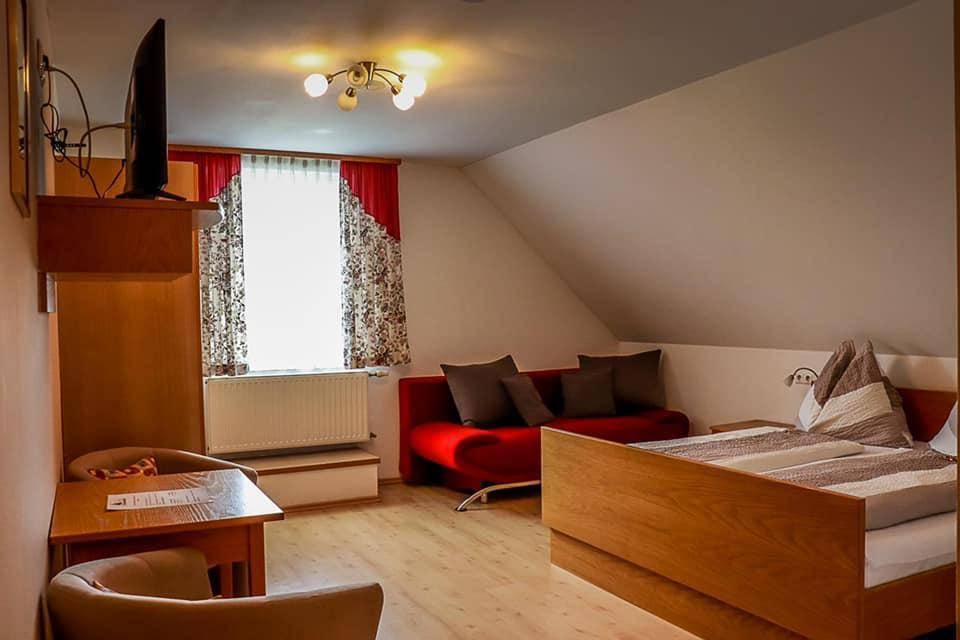 Geräumiges Schlafzimmer im Dachgeschoss mit Doppelbett, rotem Sofa, Tisch und Fernseher an der Wand.