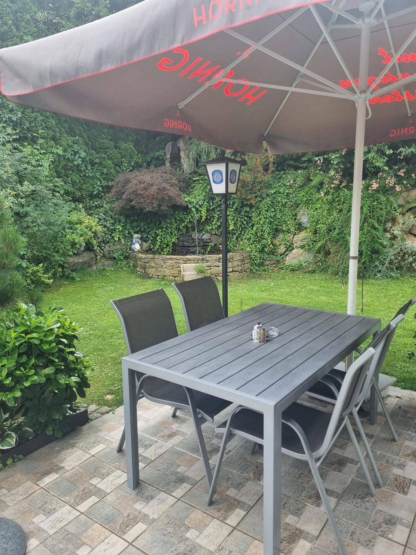 Gemütliche Terrasse mit Esstisch und Stühlen, umgeben von üppigem Grün und einem kleinen Wasserfall im Hintergrund.