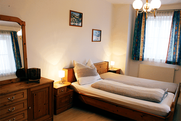 Gemütliches Schlafzimmer mit zwei Einzelbetten, Holzmöbeln, Spiegel und Bildern an der Wand.