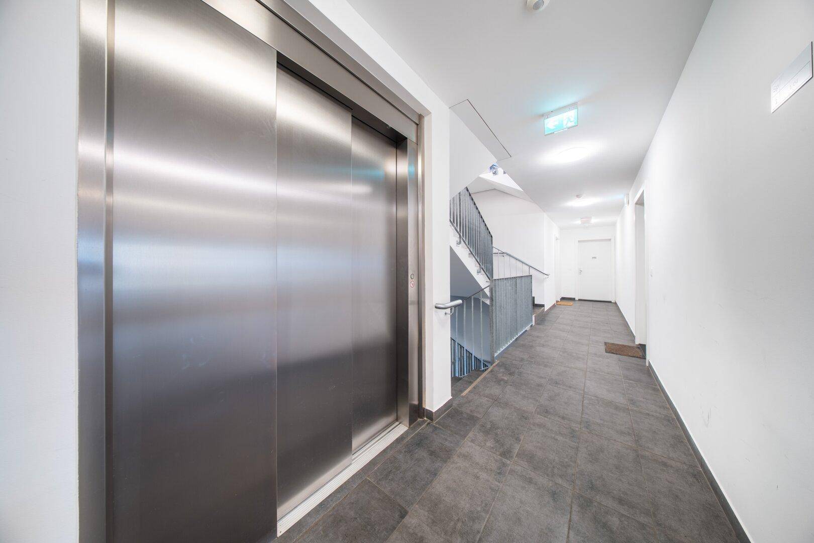 Heller Flur im Gebäude mit modernem Aufzug und Treppenhaus, gut beleuchtet.