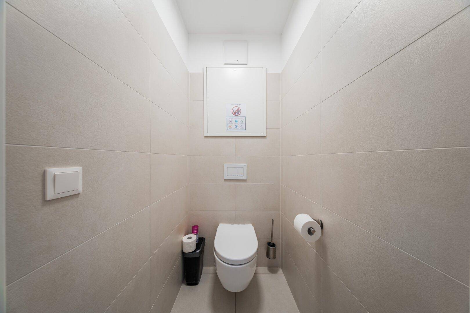 Separates WC mit wandmontierter Toilette und hellen Fliesen in einem schlichten Design.