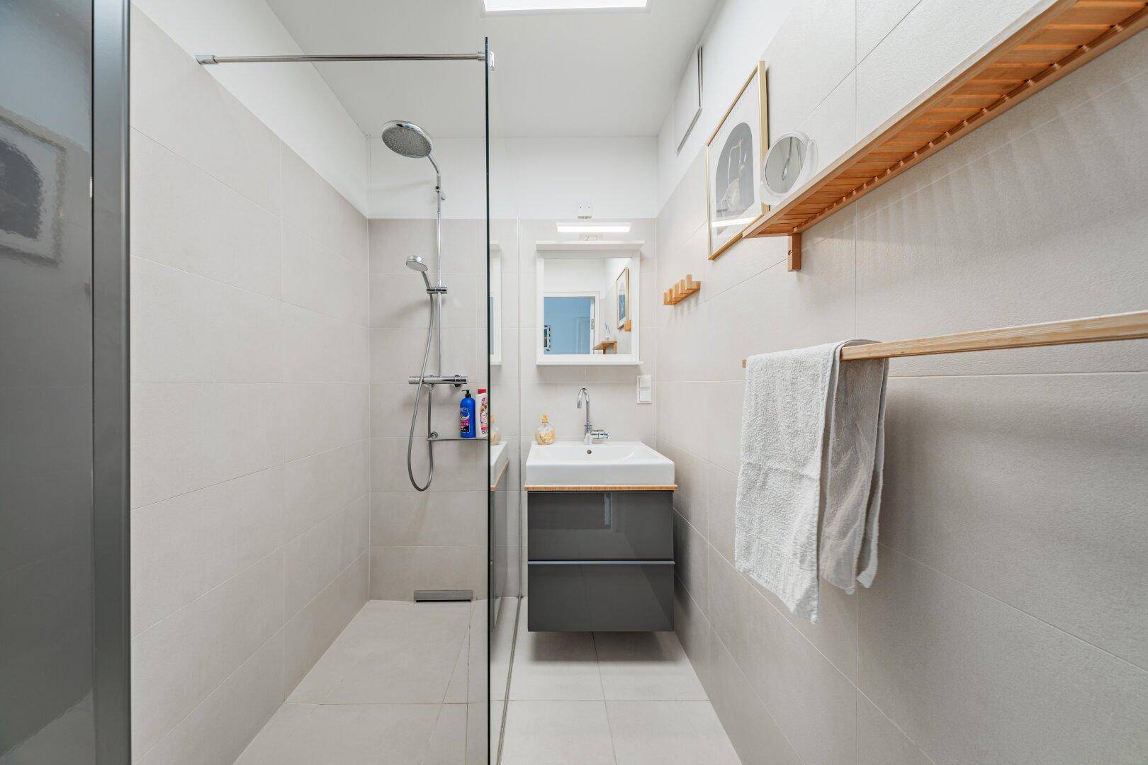 Modernes Badezimmer mit begehbarer Dusche, hellen Fliesen und einem einzelnen Waschbecken.