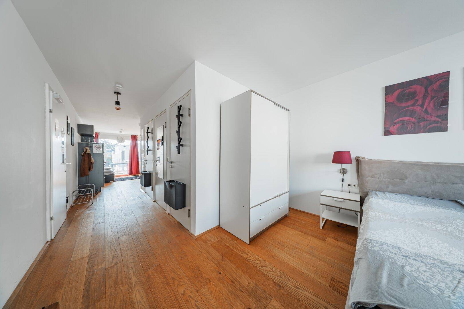 Schlafzimmer mit Holzboden und angrenzendem Flur, der zu weiteren Räumen führt.