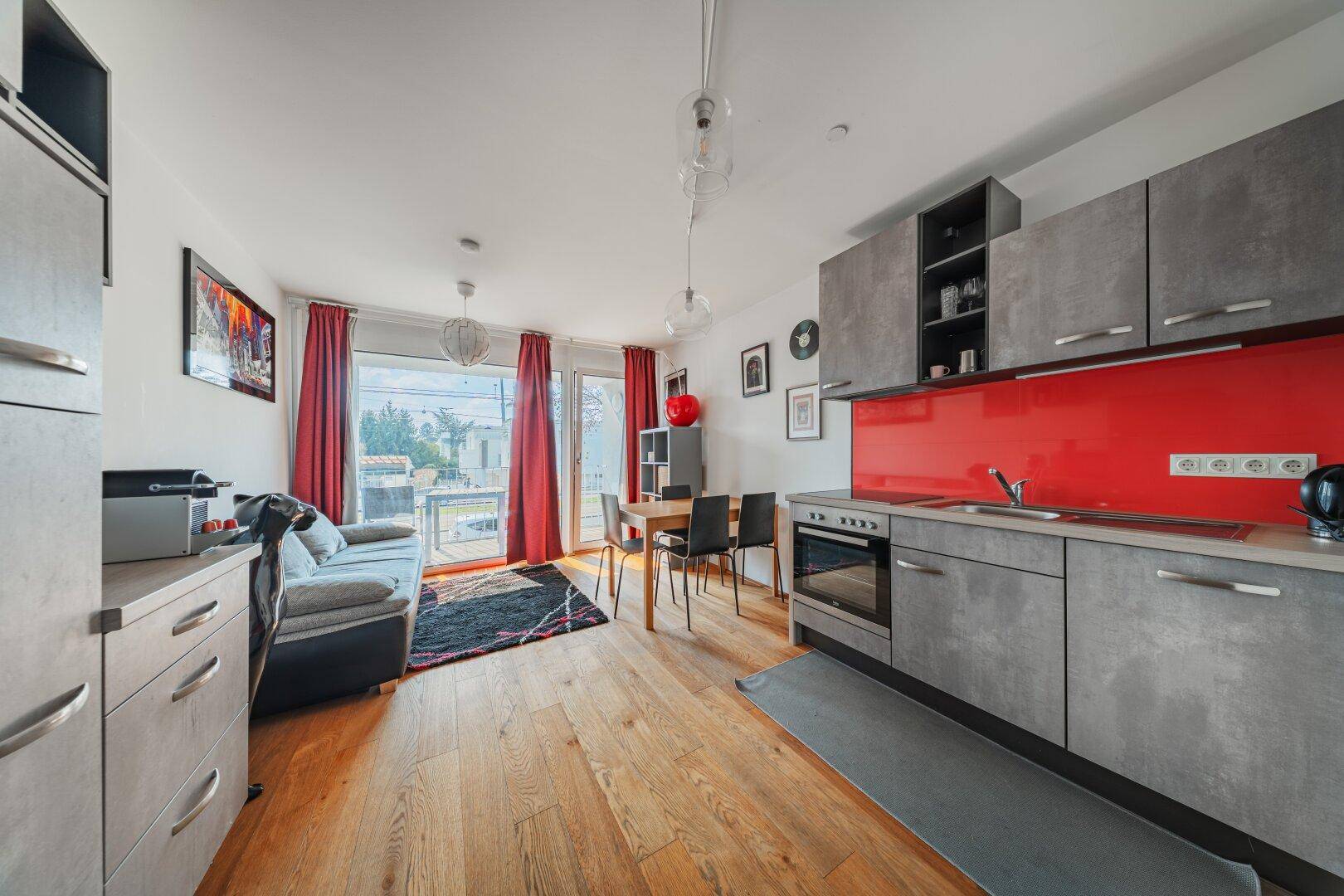 Heller Wohn- und Essbereich mit integrierter Küchenzeile, Holzboden und Zugang zum Balkon.