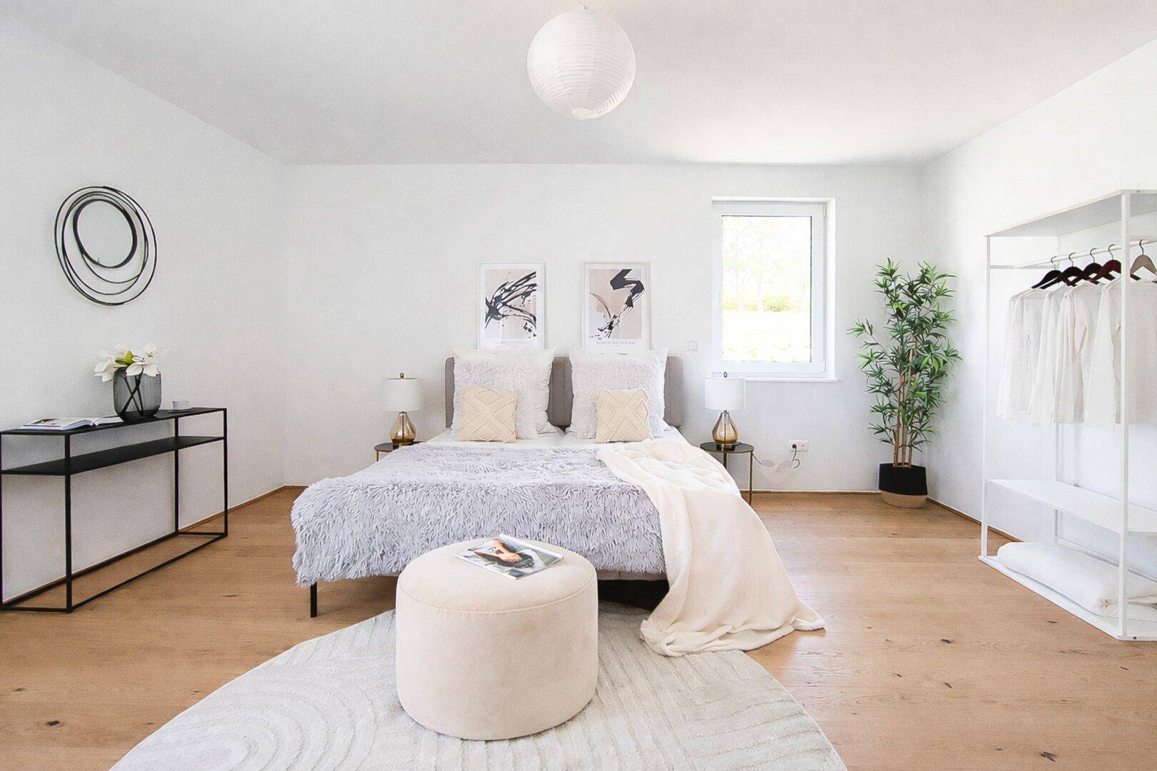 Helles Schlafzimmer mit Holzboden, großem Fenster und offenem Kleiderschrank.