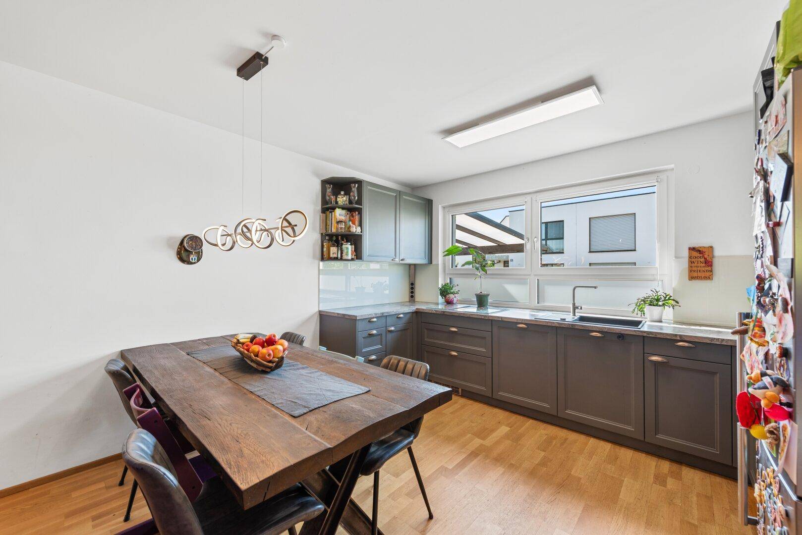 Moderne Küche mit grauen Schränken, Holztisch und Essbereich, ideal für Familienmahlzeiten.