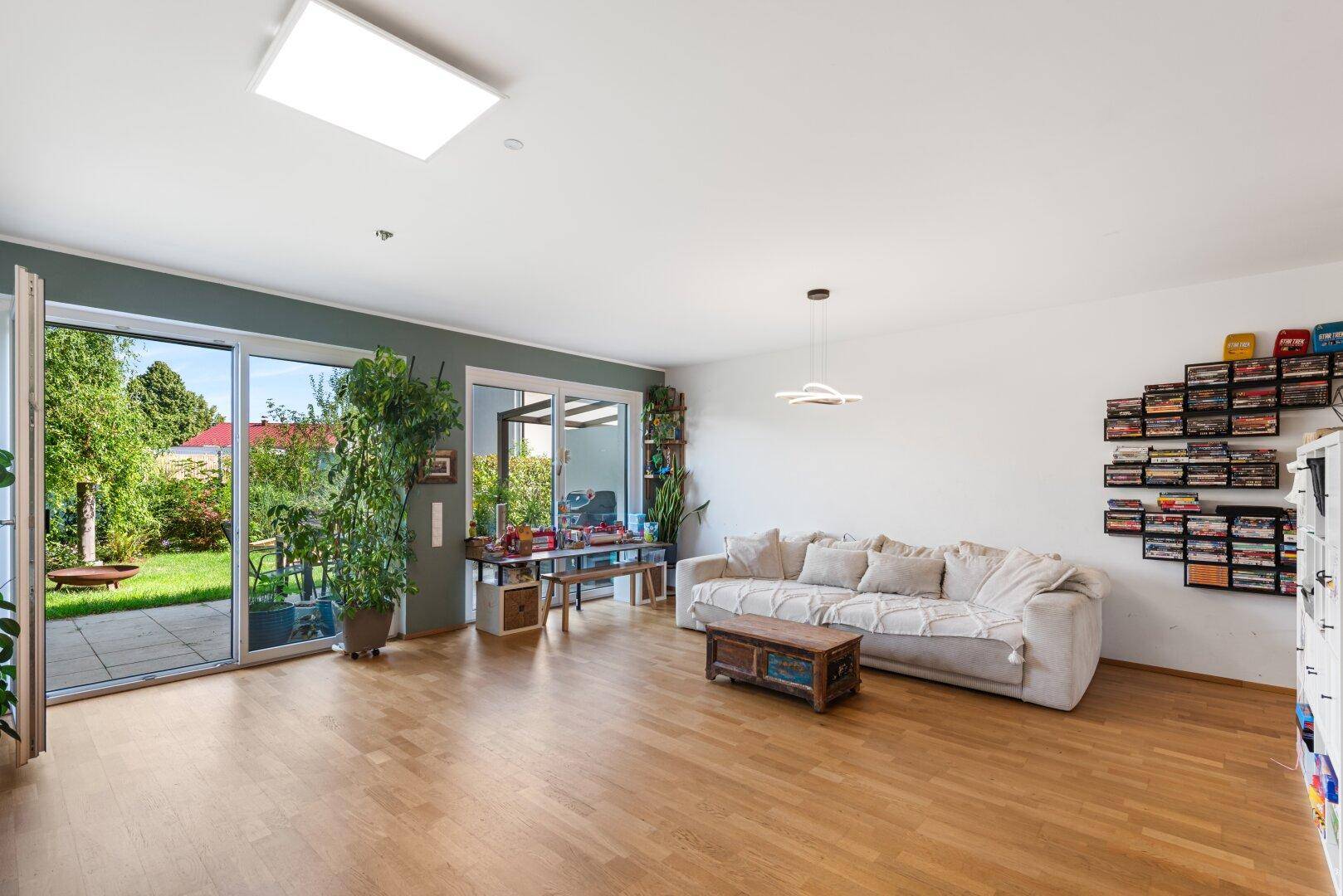 Helles Wohnzimmer mit Holzboden, bequemer Couch und Zugang zum grünen Gartenbereich.