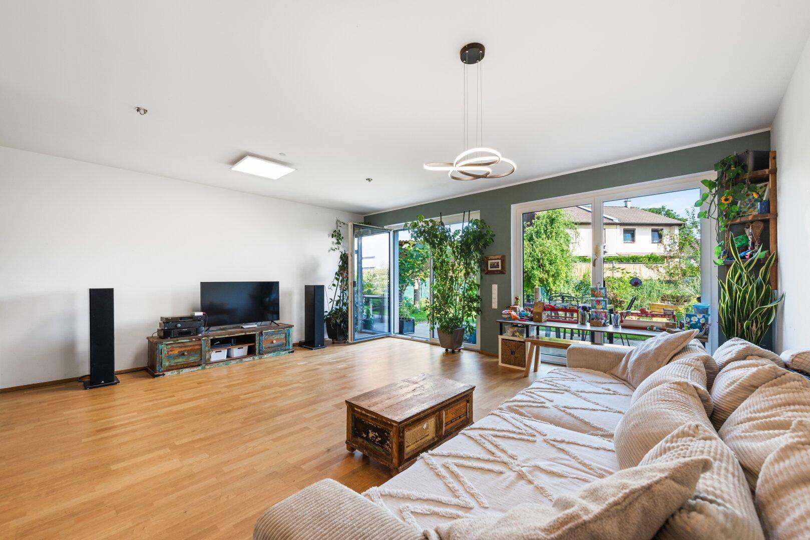 Geräumiges Wohnzimmer mit Fernseher, Holzboden und großen Fenstern zum Garten.