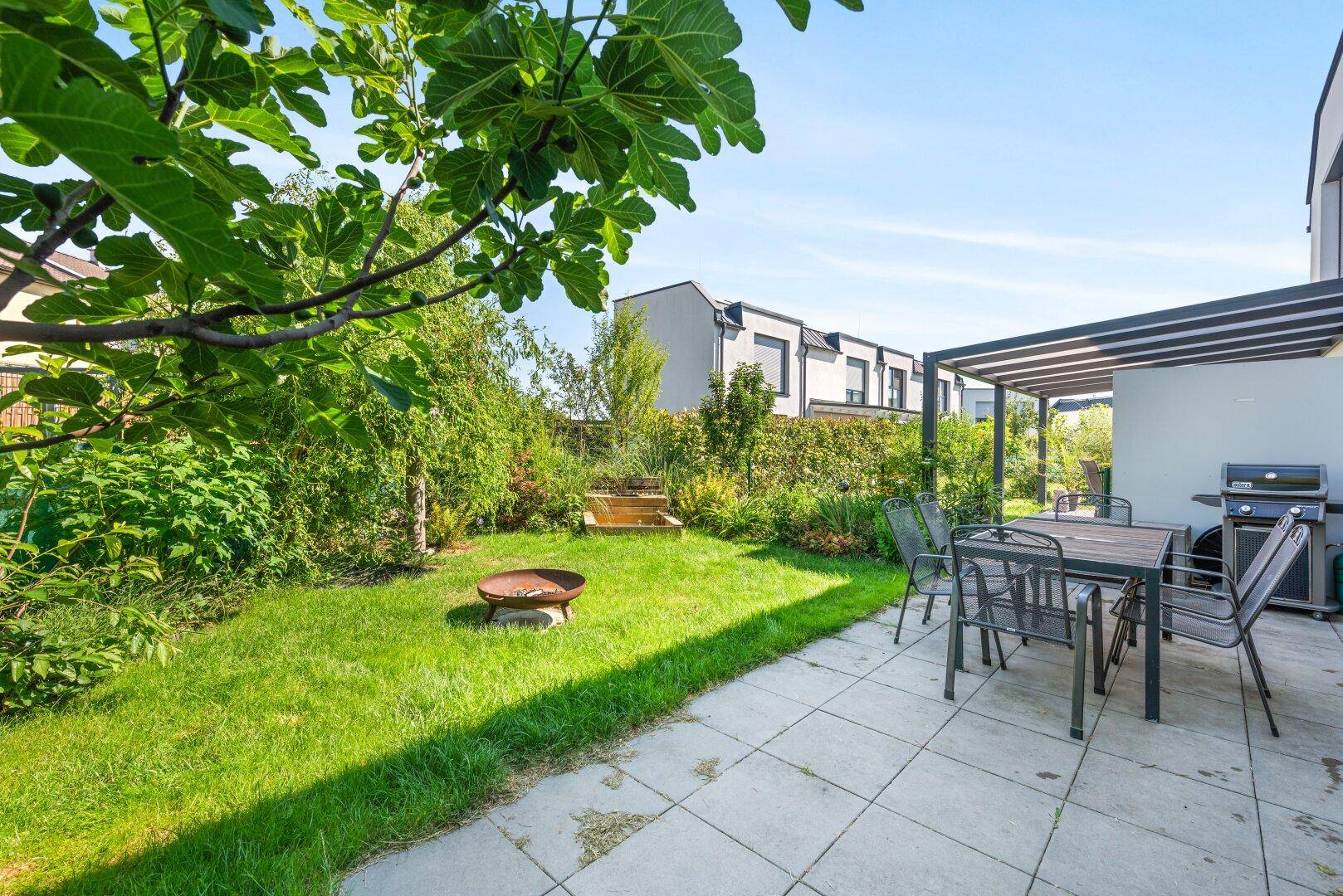 Gepflegter Gartenbereich mit überdachter Terrasse, Grillplatz und üppiger Bepflanzung.