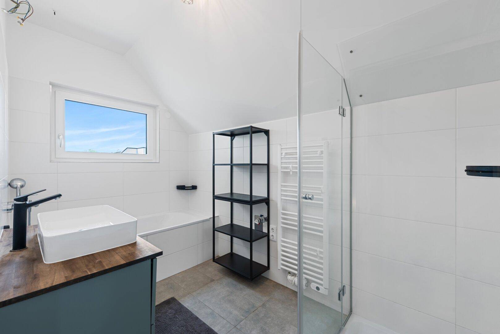 Modernes Badezimmer mit Badewanne, Dusche, Waschbecken und Fenster unter Dachschräge.