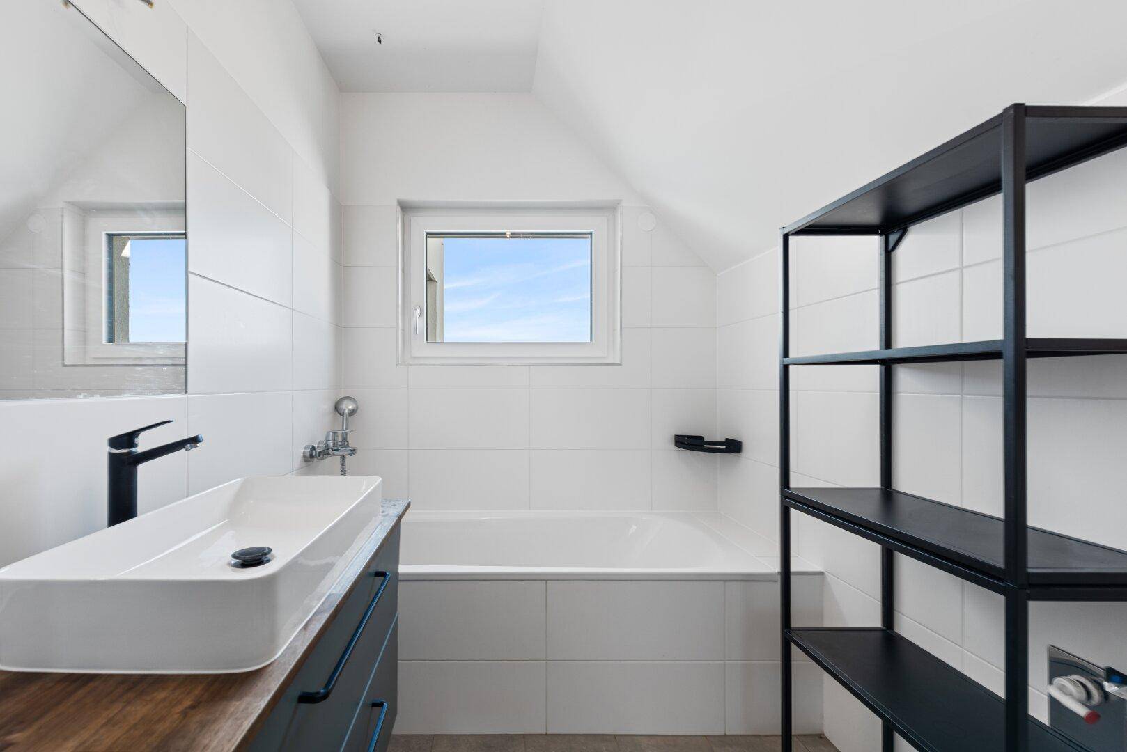 Helles Badezimmer mit moderner Badewanne, Waschbecken und Fenster für natürliche Belüftung.