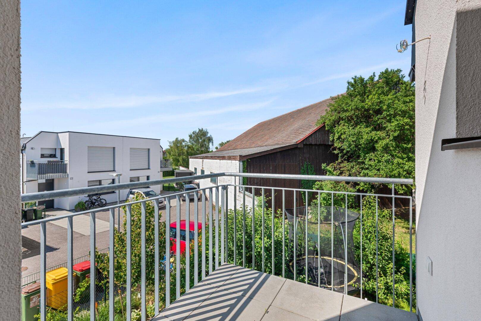 Kleiner Balkon mit Metallgeländer und Ausblick auf die Nachbarschaft und grüne Umgebung.