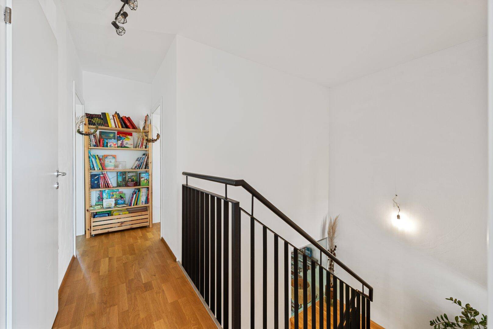 Flur im Obergeschoss mit Holzboden, Bücherregal und Blick auf den Treppenbereich.
