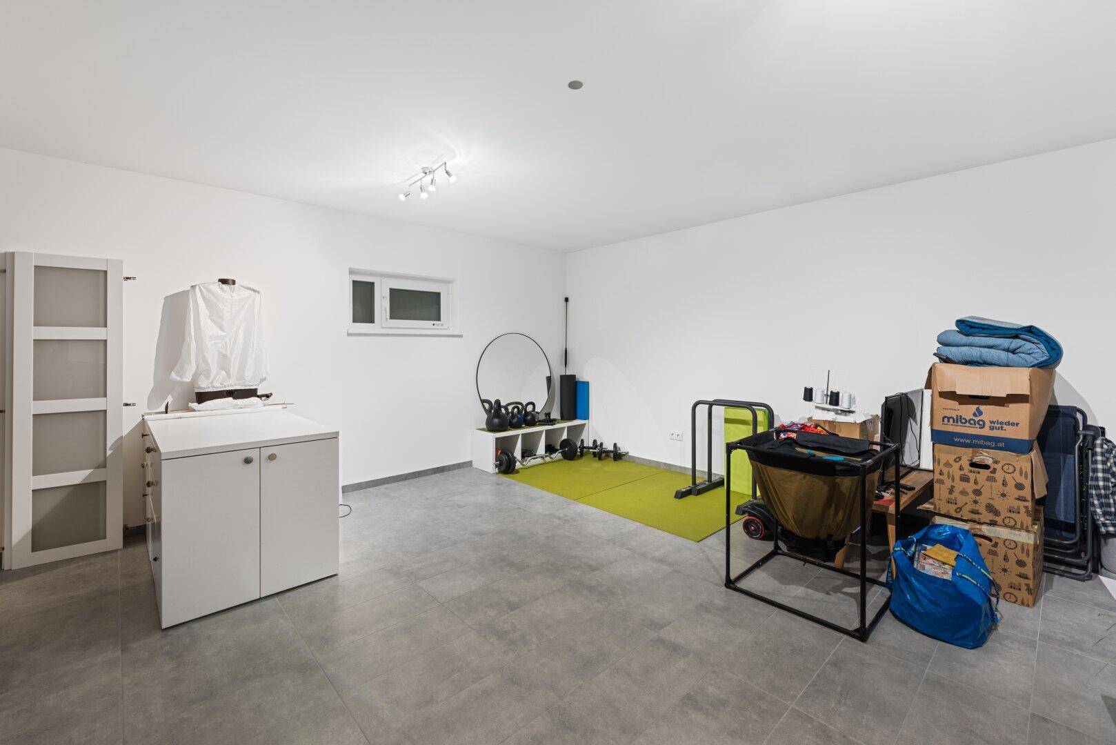 Vielseitiger Kellerraum mit Fliesenboden, genutzt als Fitness- und Abstellbereich.