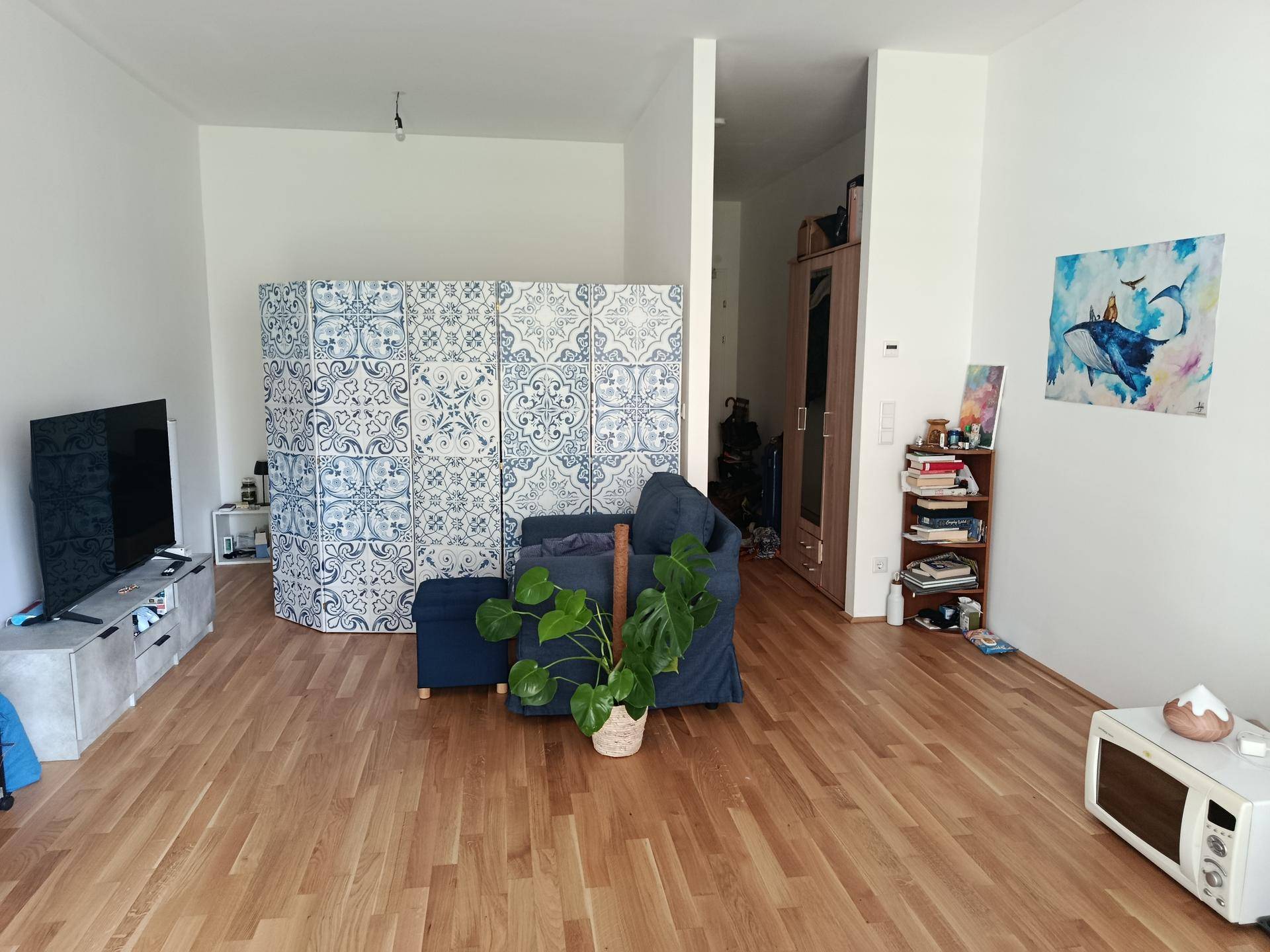 Geräumiges Wohnzimmer mit Holzboden, einem dekorativen Raumteiler und moderner Einrichtung.