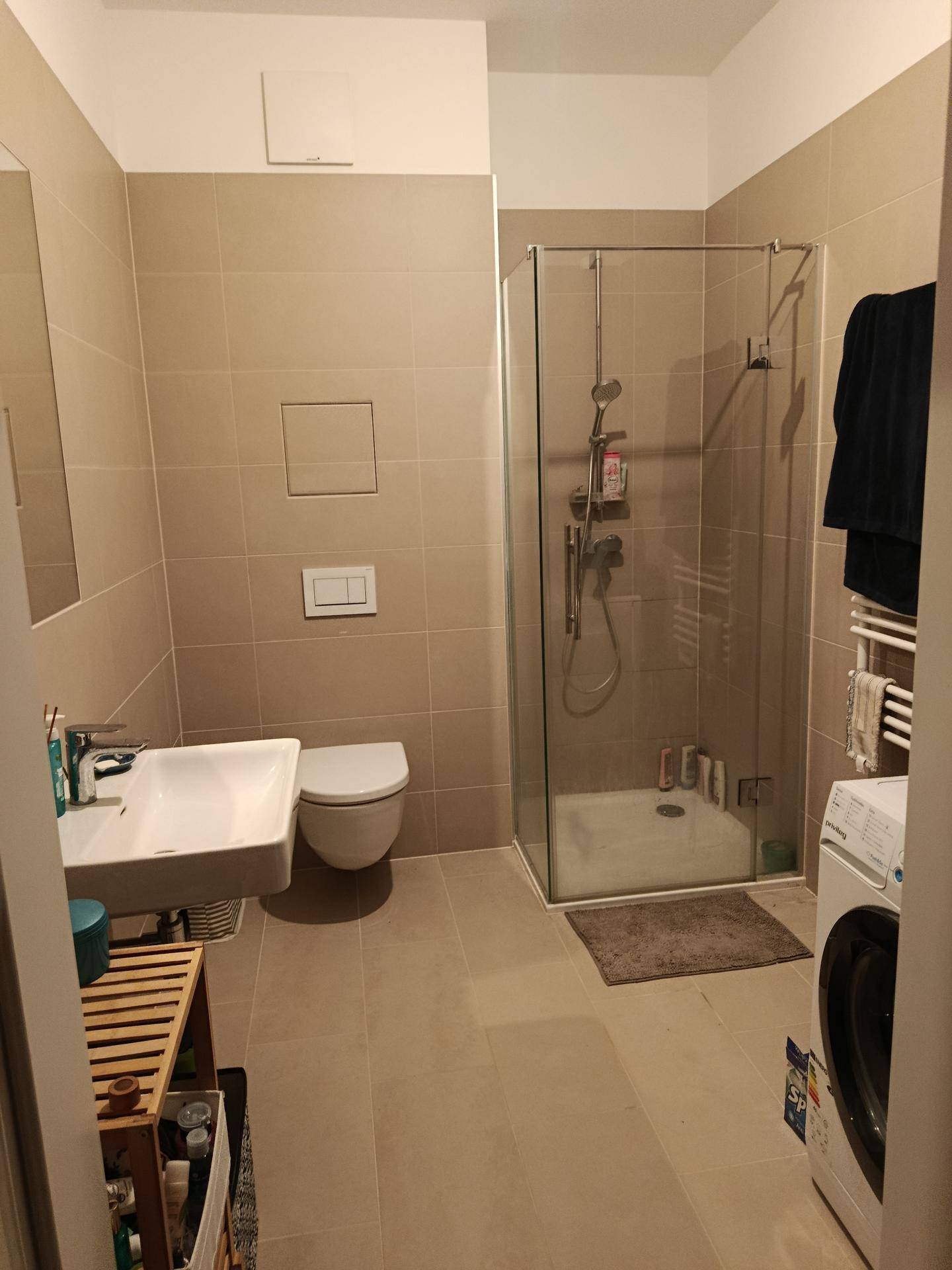 Modernes Badezimmer mit beigefarbenen Fliesen, Duschkabine, WC und Waschbecken.