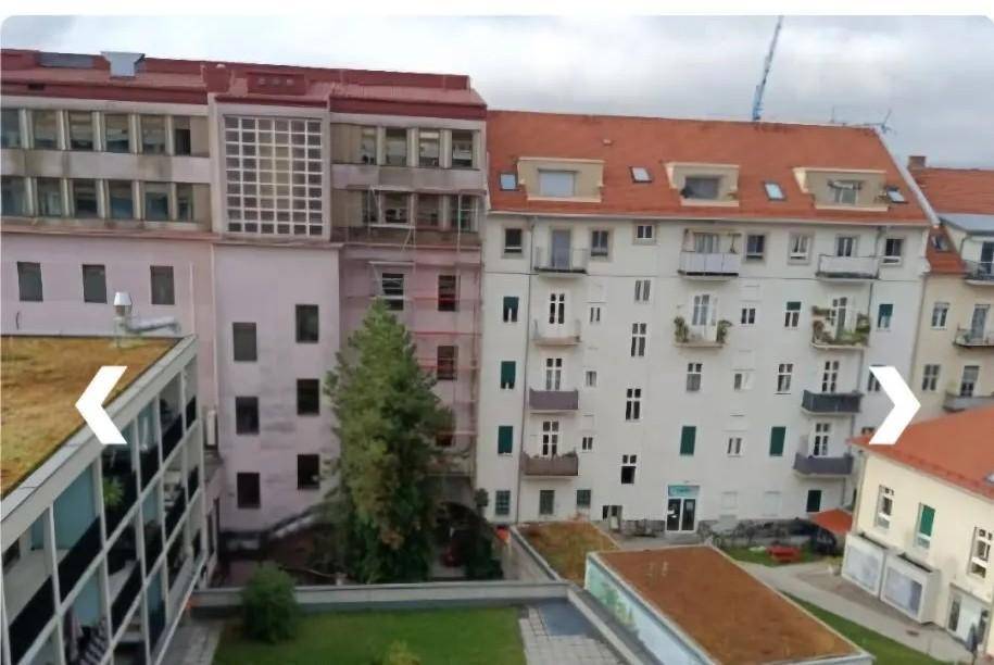 Ansicht von mehreren Gebäuden mit unterschiedlichen Fassaden und Dachformen in städtischer Umgebung, mit Grünflächen.