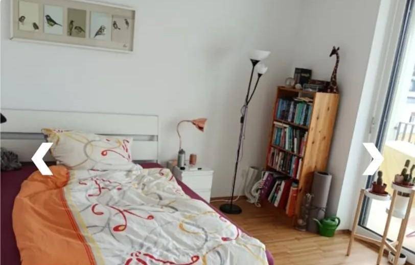 Gemütliches Schlafzimmer mit Holzboden, Bücherregal und Zugang zu einem kleinen Balkon für frische Luft.