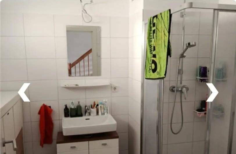 Modernes Badezimmer mit weißen Fliesen, Duschkabine und einem Waschbecken mit Unterschrank für Stauraum.