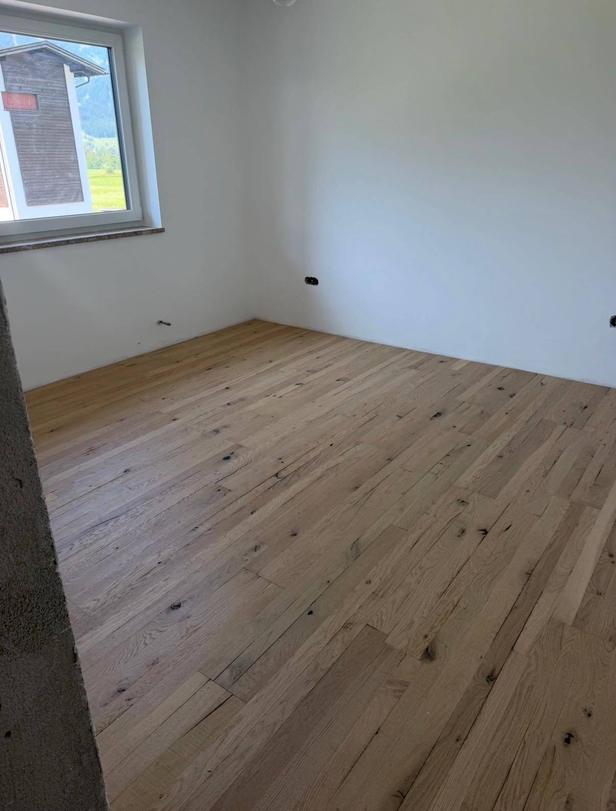 Unmöblierter Raum im Bau mit neuem Holzboden und Fenster.