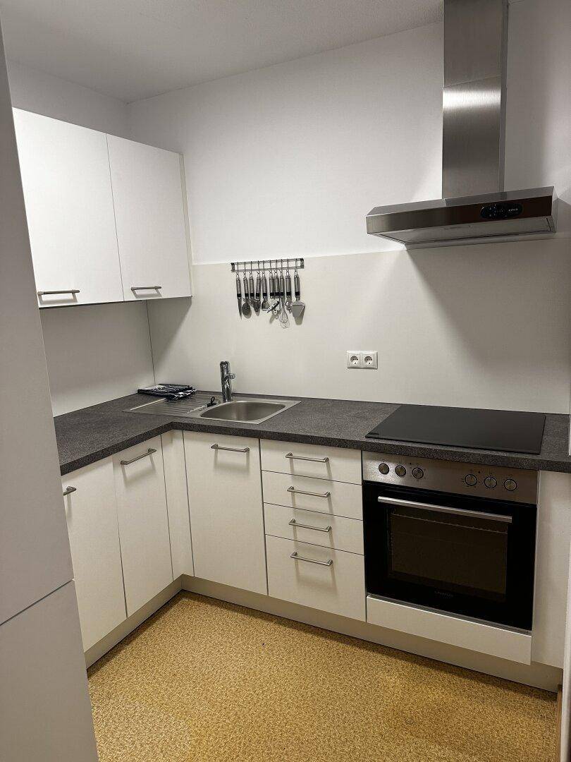 Moderne Einbauküche mit weißen Schränken, dunkler Arbeitsplatte und integrierten Geräten.