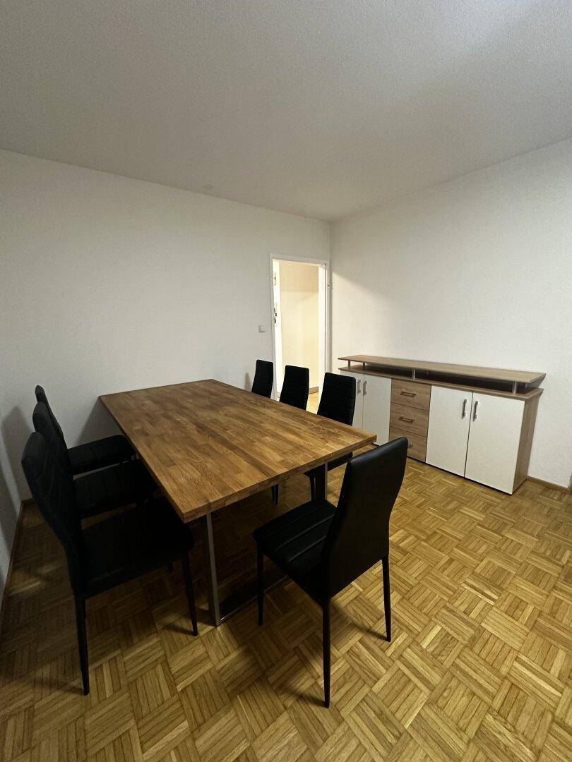 Geräumiger Essbereich mit Holztisch, schwarzen Stühlen und Parkettboden.